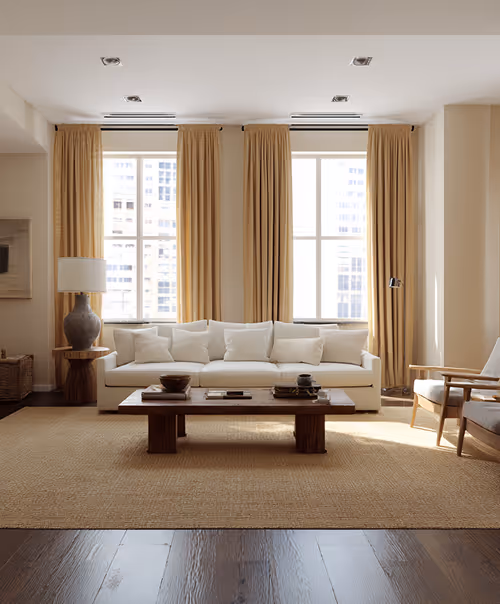 Un salon moderne avec deux grandes fenêtres, un design minimaliste, des sols et des meubles en bois chaleureux, alliance réussie du confort et de l’élégance architecturale.