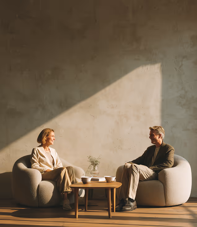 Deux personnes assises dans une pièce lumineuse et minimaliste, baignée de lumière naturelle, qui illustre un aménagement soigné et une esthétique architecturale moderne.
